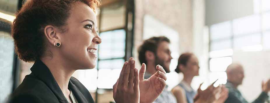 A group of people seated indoors applauding during a presentation or group discussion in a bright, modern workspace.