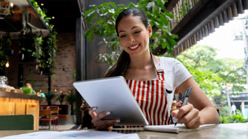 A small business owner wearing a striped apron cheerfully viewing their tablet