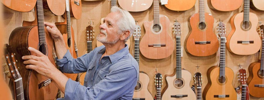 Elderly man in a music instrument store with wooden guitars in background