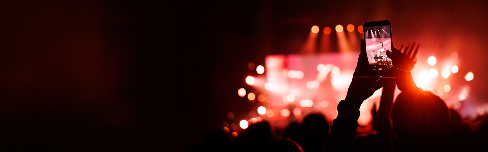 Person recording a live concert on a smartphone amid bright stage lights.