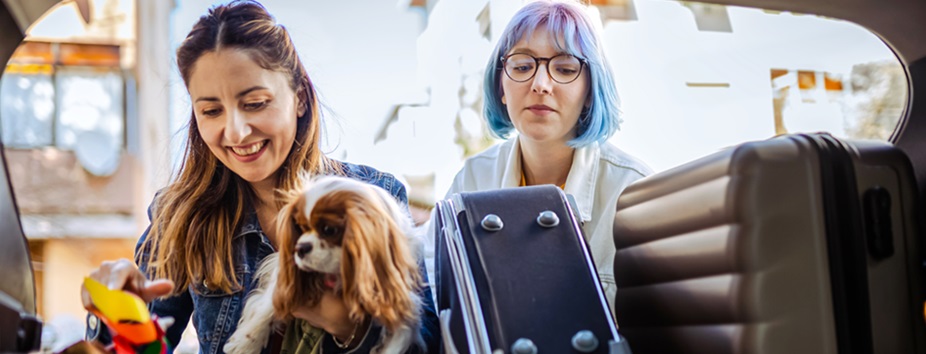 Two young women are loading luggage into the back of a car. They are taking a long-awaited road trip after one of them decided to explore their car finance options, which allowed them to buy their first car. 