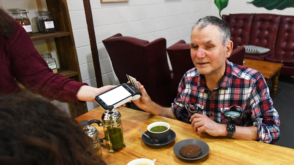 Photo of Peter Greco, in a cafe, tapping his payment card to use Westpac's new EFTPOS payment terminal.