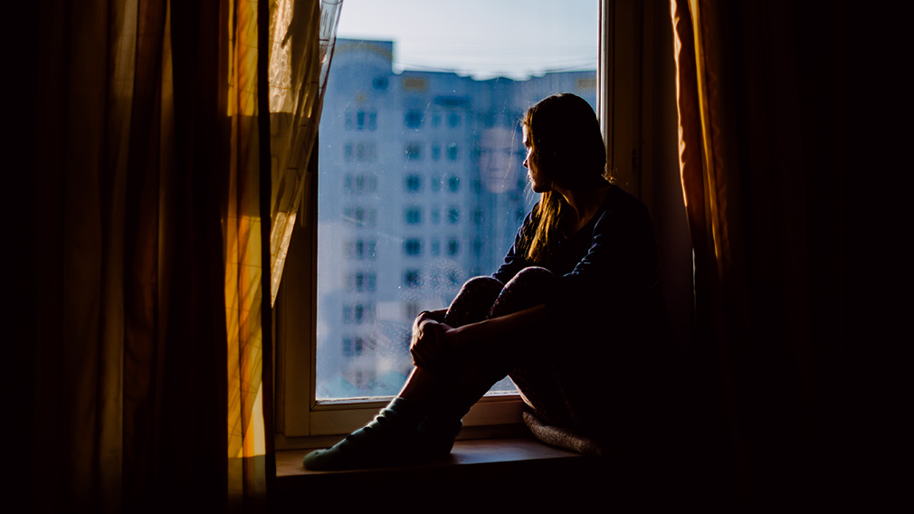 An image of a sad woman sitting staring out a window, representing the grief felt by parents who suffer early pregancy loss. 